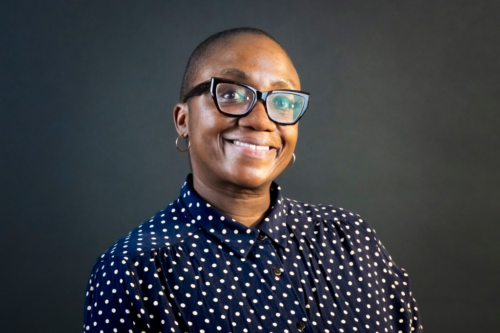 Headshot of a woman with short hair, eyeglasses wearing a blue blouse with tan polka dots. She is smiling in the image.